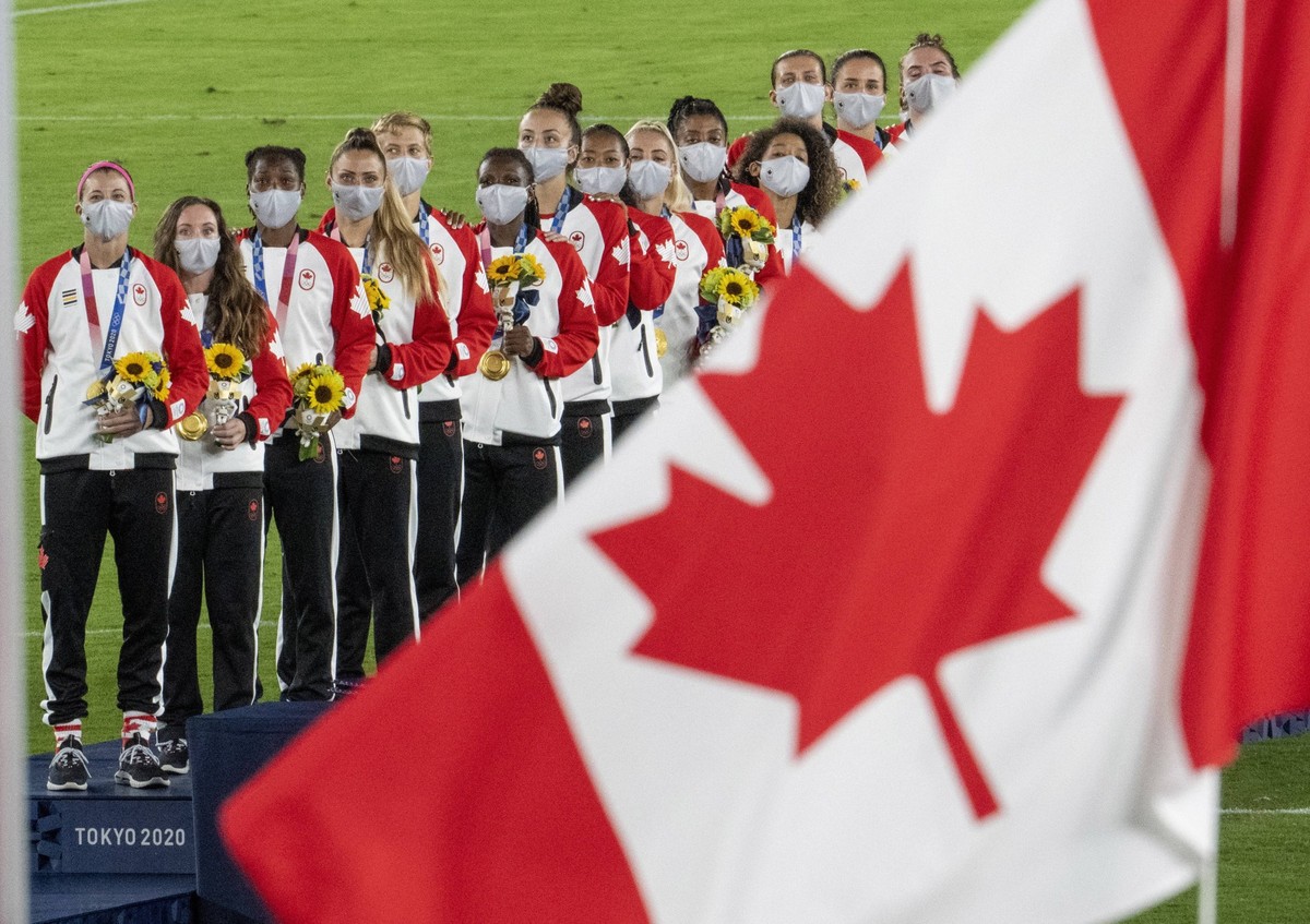 August 6, 2021, Tokyo, JAPAN: Members of the Canadian women��� s soccer team watch the flag raise after being presented with their gold medals at the Tokyo Olympics in Tokyo, Japan on Friday August 6, ...