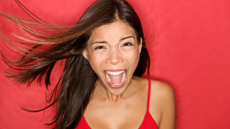 Scream. Woman screaming wild and crazy at full energy looking at camera on red background. Beautiful mixed race Asian Caucasian brunette female model with wind in the hair.
Horror, Angst, Schrei