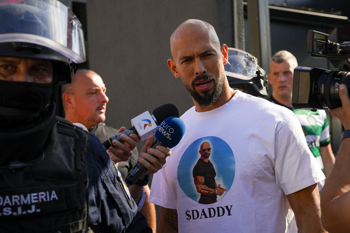 Andrew Tate talks to media as he is being led for questioning after a police search raid on his residence, on the outskirts of Bucharest, Romania, Wednesday, Aug. 21 2024. Masked police officers in Ro ...