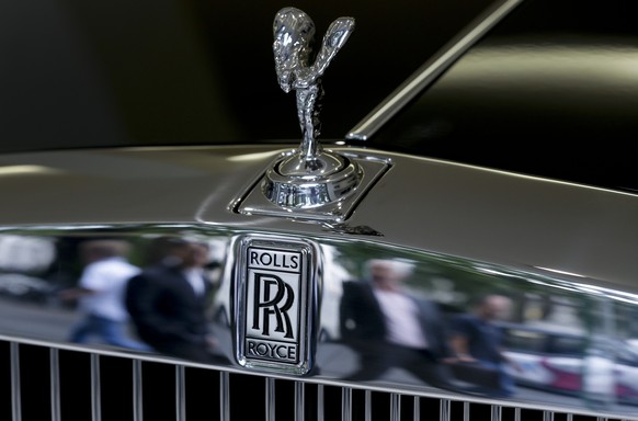 Pedestrians are reflected in the chrome work under The Spirit of Ecstasy on the front of a Rolls- Royce car, in a show room in London, Tuesday, July 8, 2014. Sales of luxury Rolls-Royce cars, which co ...