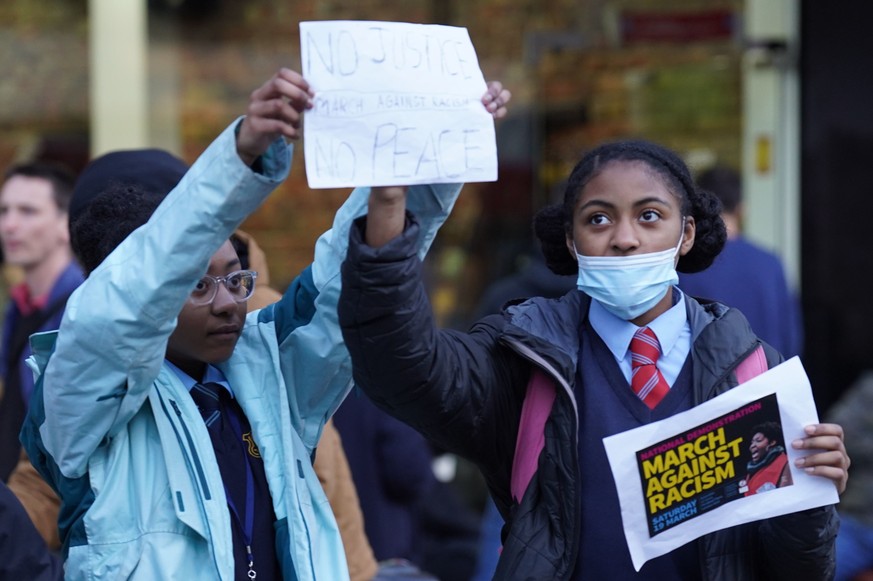 School children hold posters as people gather outside Stoke Newington Police Station to protest over the treatment of a black 15-year-old schoolgirl who was strip-searched by police, in London, Friday ...