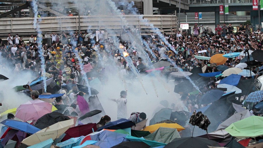 In this Sunday, Sept. 28, 2014, file photo, riot police launch tear gas into the crowd as thousands of protesters surround the government headquarters in Hong Kong. Hong Kong police used tear gas on S ...