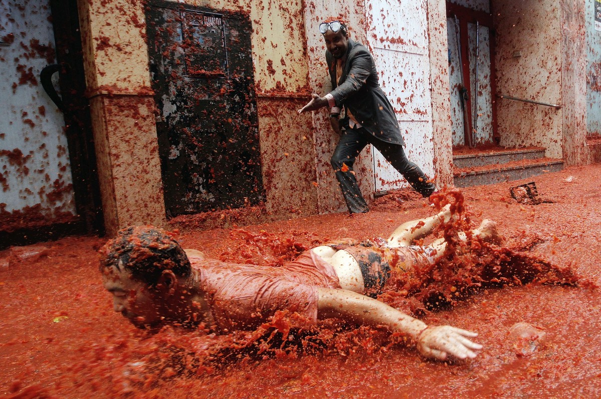 epa06171489 A man slides on the pavement covered with squashed tomatoes as he takes part in the traditional tomato fight called 'Tomatina' in Bunol, Spain, 30 August 2017. As every year on t ...