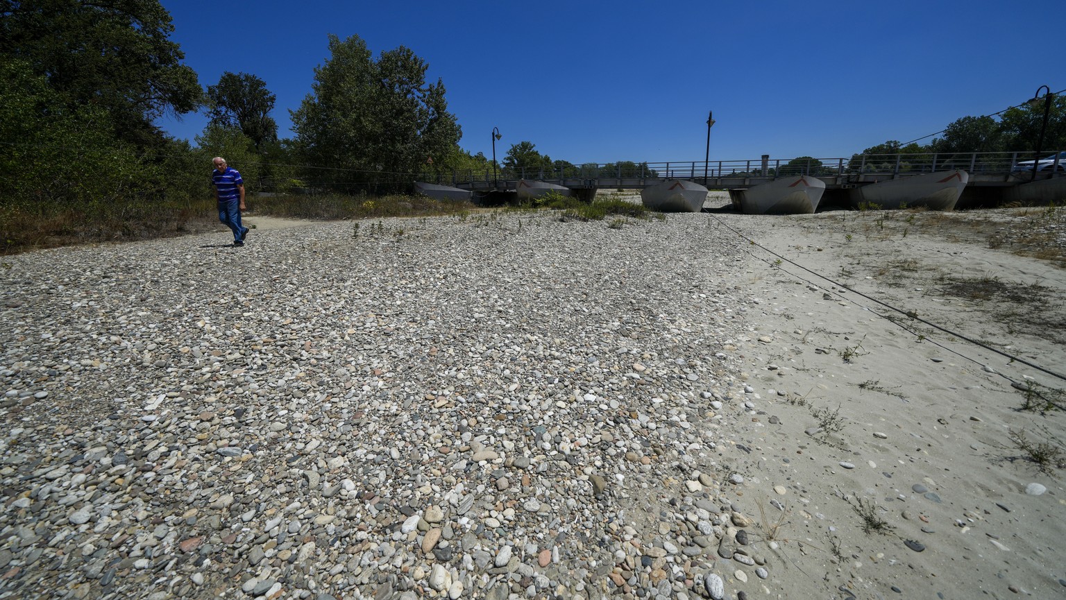 A man walks on the dry-out side of the riverbed of the Ticino river near Bereguardo, some 25 kilometers south of of Milan in northern Italy, Friday, July 8, 2022. The Italian government declared a sta ...