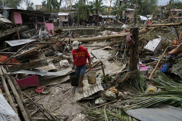 A man carries pails beside damaged homes due to Typhoon Rai in Talisay, Cebu province, central Philippines on Friday, Dec. 17, 2021. A strong typhoon engulfed villages in floods that trapped residents ...