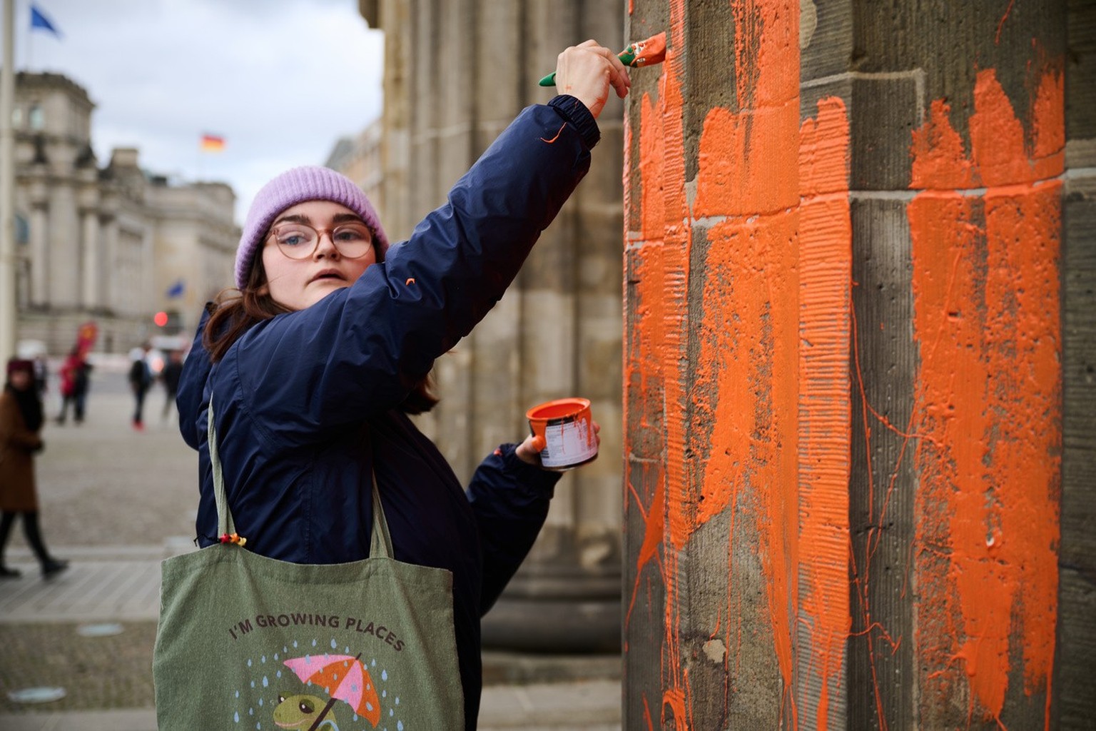 16.11.2023, Berlin: Eine Klimaaktivistin bemalt das Brandenburger Tor mit oranger Farbe. Die Gruppe Letzte Generation teilte am Donnerstag mit, dass Mitglieder mit Pinseln die Westseite des Bauwerks e ...