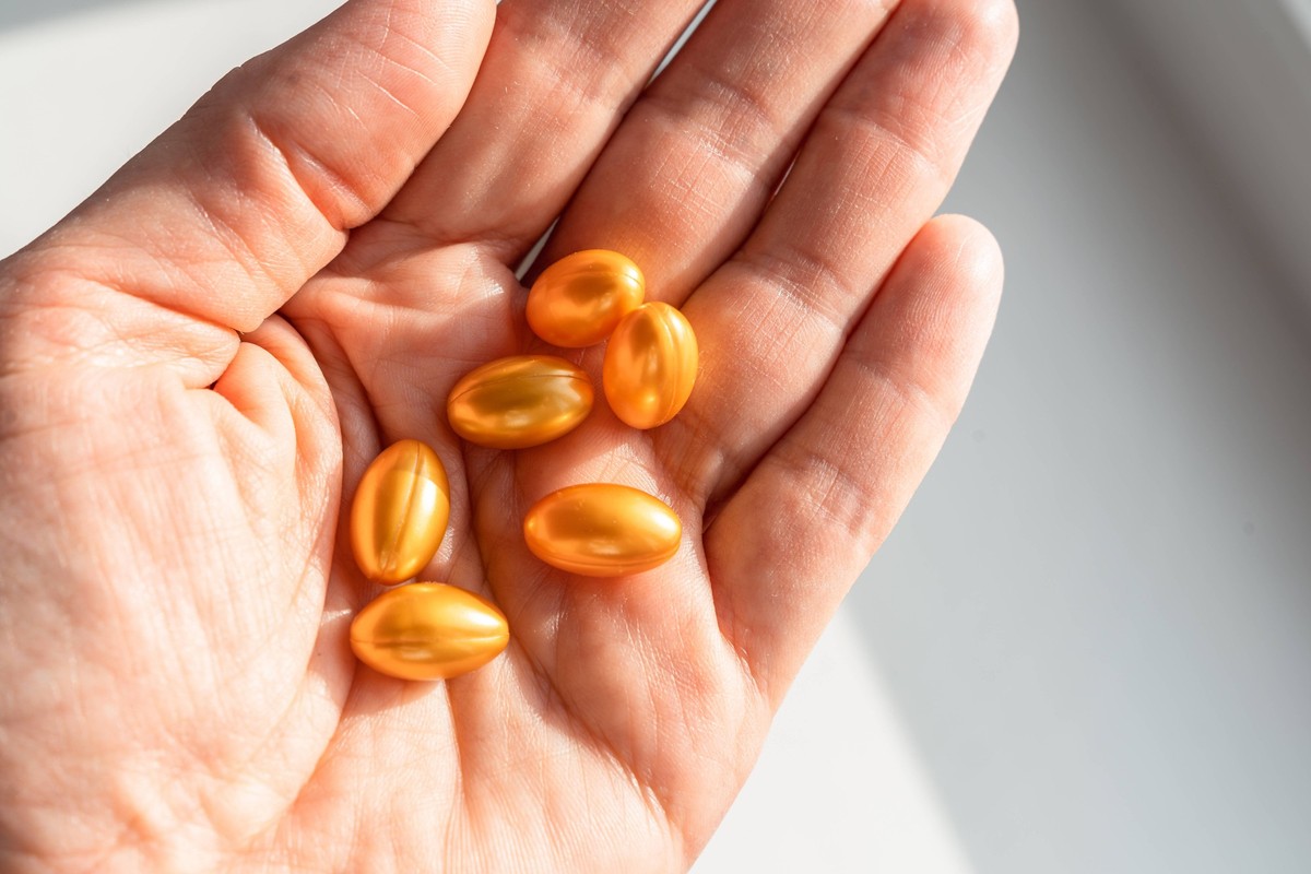 Eine Hand hält glänzende, goldene Softgel-Kapseln, die Nahrungsergänzungsmittel, Vitamine und Medikamente für Gesundheit, Schönheit und Wohlbefinden symbolisieren. Gesunder Lebensstil, Selbstfürsorge  ...