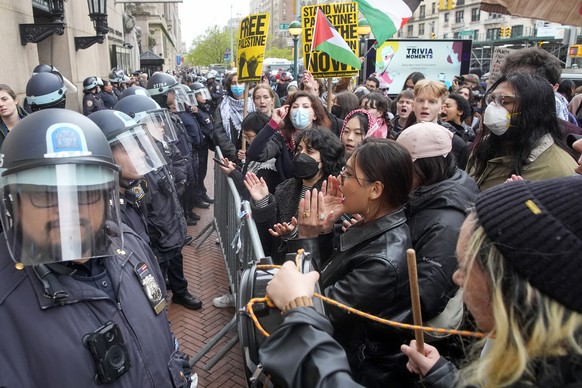 New York City police officers in riot gear stand guard as demonstrators chant slogans outside the Columbia University campus, Thursday, April 18, 2024, in New York. The protesters were calling for the ...
