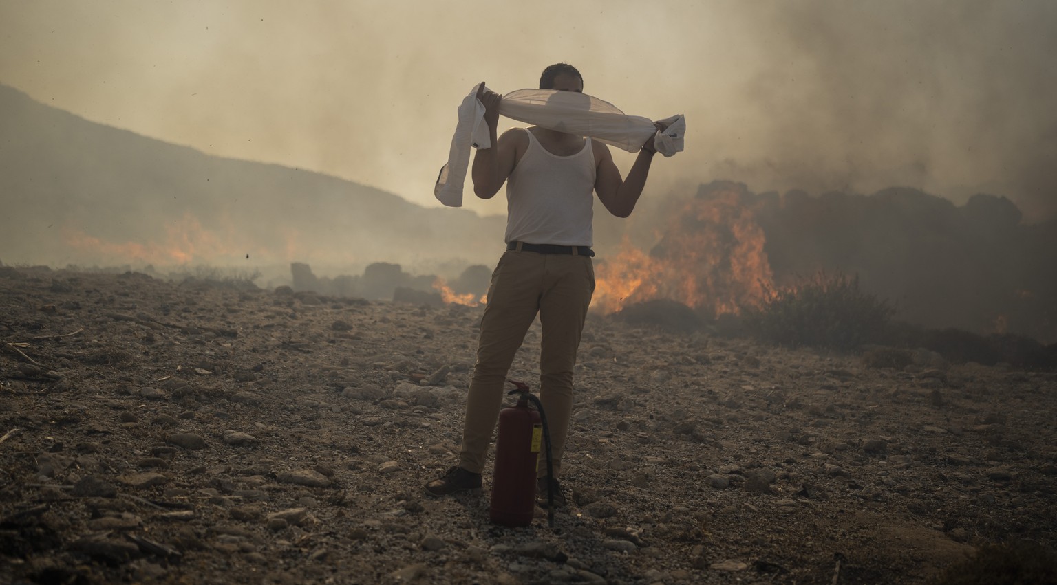 FILE - A man wraps his shirt over his face as he tries to extinguish a fire, near the seaside resort of Lindos, on the Aegean Sea island of Rhodes, southeastern Greece, on July 24, 2023. Europe is fac ...