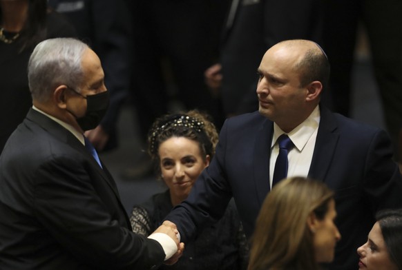 Israel's new prime minister Naftali Bennett shakes hands with outgoing prime minister Benjamin Netanyahu during a Knesset session in Jerusalem Sunday, June 13, 2021. Israel's parliament has voted in f ...
