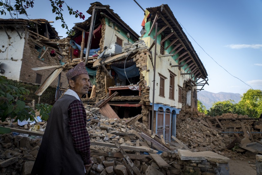 A man stands in front of his earthquake-damaged house in Jajarkot district, northwestern Nepal, Sunday, November 5, 2023. Most houses in villages in Jajarkot district have collapsed or been seriously damaged.