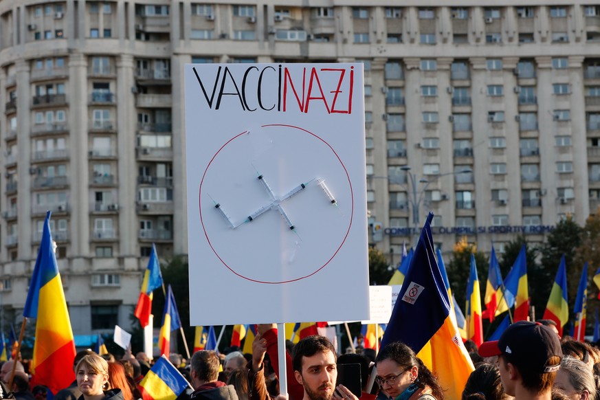 epa09502283 A man holding a banner attends with syringes in the shape of a Swastika during a protest against new measures ordered by the Romanian government during the fourth wave of the Covid-19 Coro ...