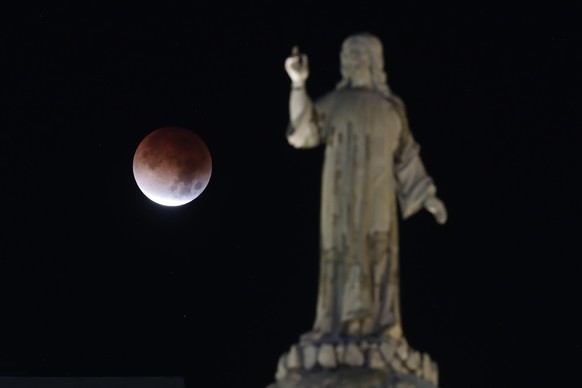 epa12791850 A stage of a total lunar eclipse appears behind a statue in San Salvador, El Salvador, 03 March 2026. The total lunar eclipse left a 'Blood Moon' that will be visible for approxi ...