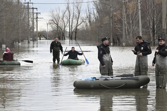 Police officers stand guarding an area as people use rubber boats in a flooded street after part of a dam burst, in Orsk, Russia. State media say Russia&#039;s government has declared the situation in ...
