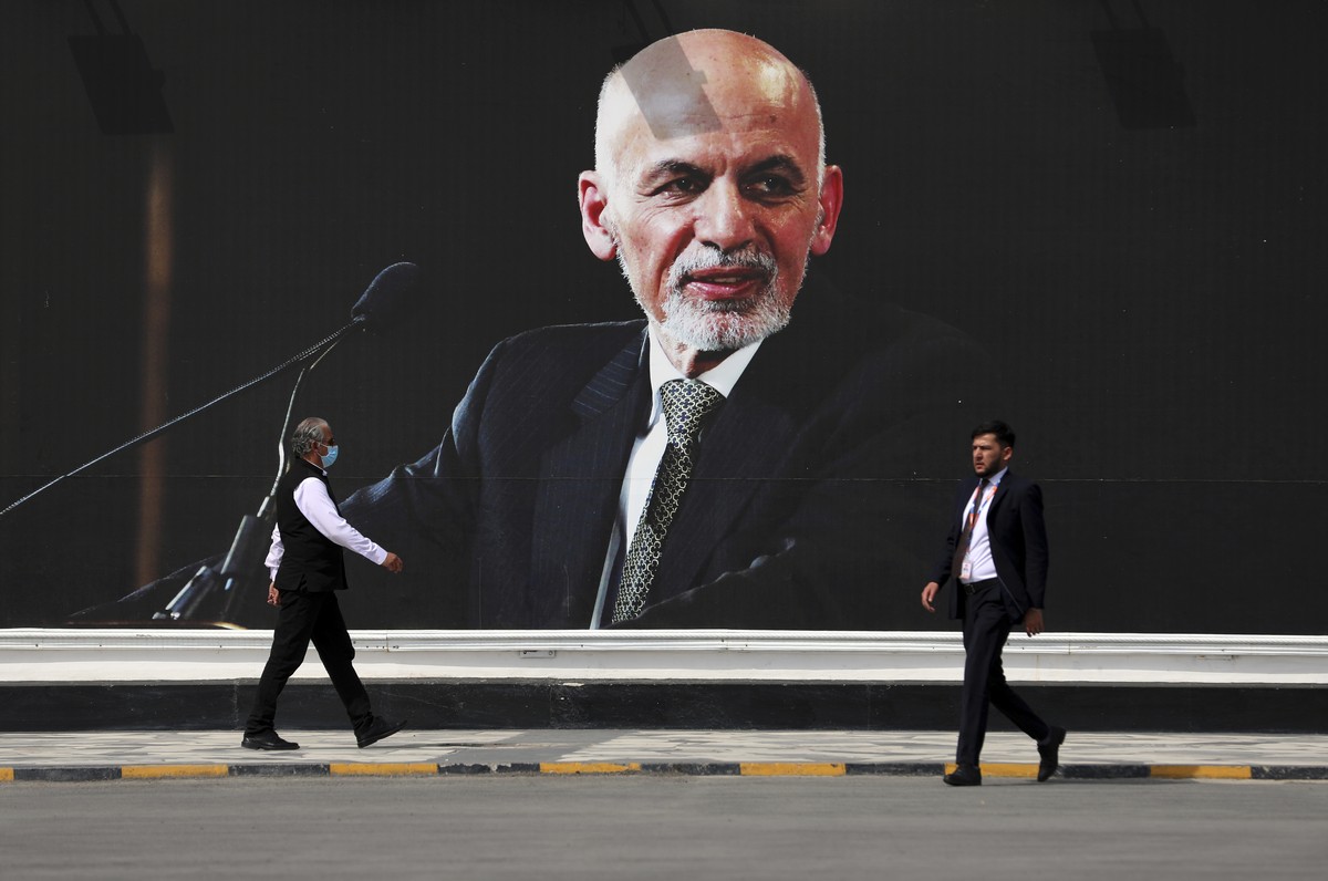 People walk near a mural of President Ashraf Ghani at Hamid Karzai International Airport, in Kabul, Afghanistan, Saturday, Aug. 14, 2021. As a Taliban offensive encircles the Afghan capital, there ...