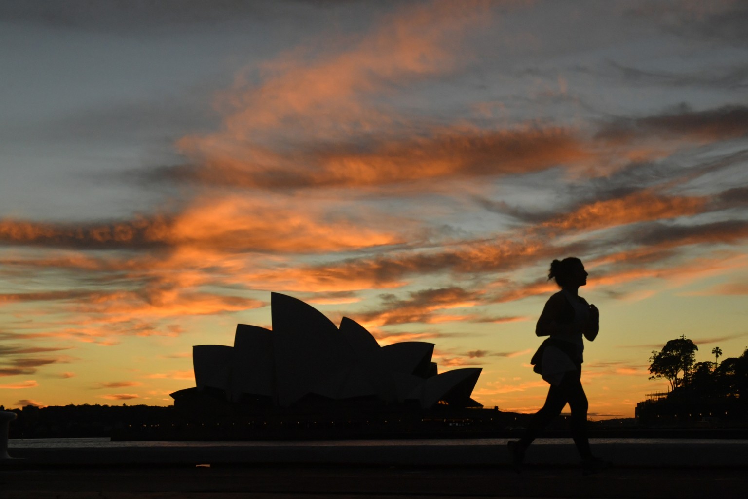 epa09352692 A jogger runs past the Sydney Opera House at dawn in Sydney, New South Wales, Australia, 19 July 2021. The stay-at-home orders for coronavirus-hit Greater Sydney and surrounds have been ti ...