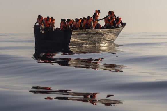 Migrants with life jackets provided by volunteers of the Ocean Viking, a migrant search and rescue ship run by NGOs SOS Mediterranee and the International Federation of Red Cross (IFCR), sit in a wood ...