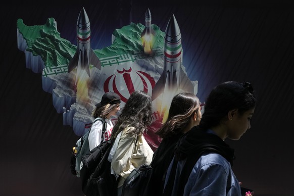Iranian women without wearing their mandatory Islamic headscarf walk past a banner showing missiles being launched from Iranian map in northern Tehran, Iran, Friday, April 19, 2024. Iran fired air def ...
