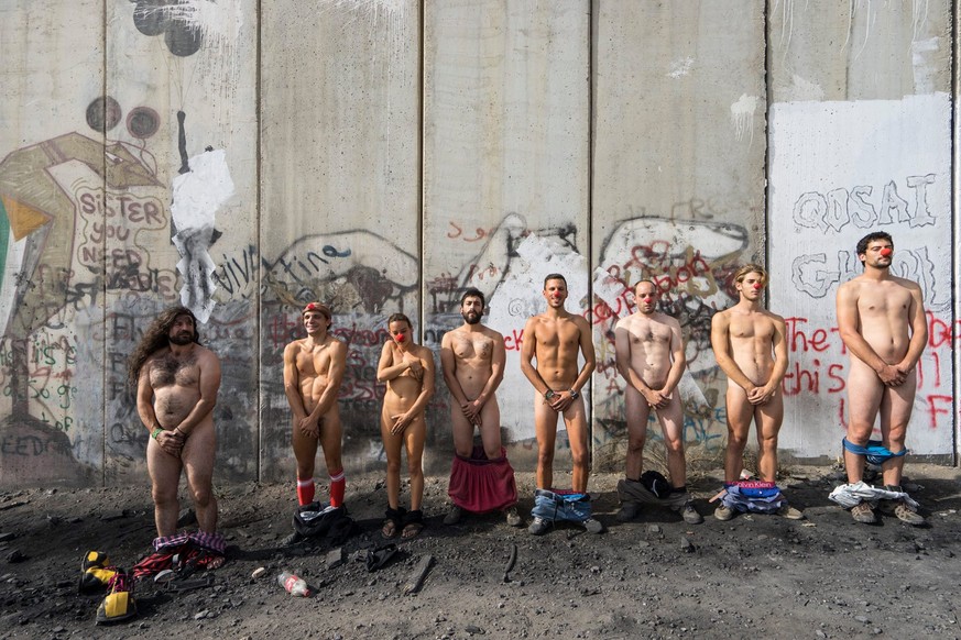 Acht nackte Clowns vor der Sperranlage, welche die Westbank von Israel trennt.