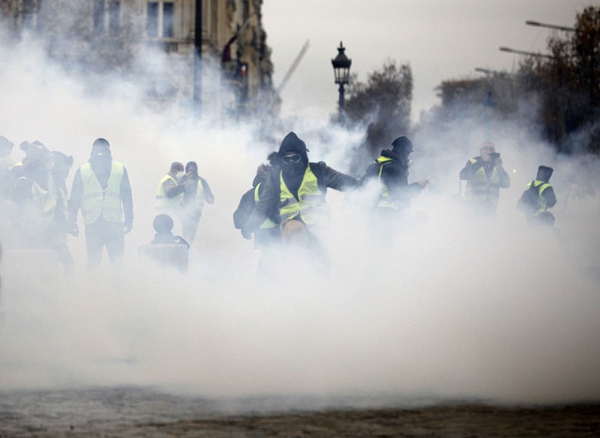 Masked demonstrators wearing yellow jackets appear through tear gas near the Champs-Elysees avenue during a demonstration Saturday, Dec. 1, 2018 in Paris. French authorities have deployed thousands of ...