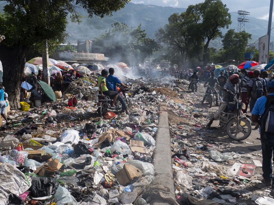 epa10231898 People move through a street covered with garbage that has not been collected, in Port-au-Prince, Haiti, 08 October 2022. The Haitian government has requested from its International partne ...