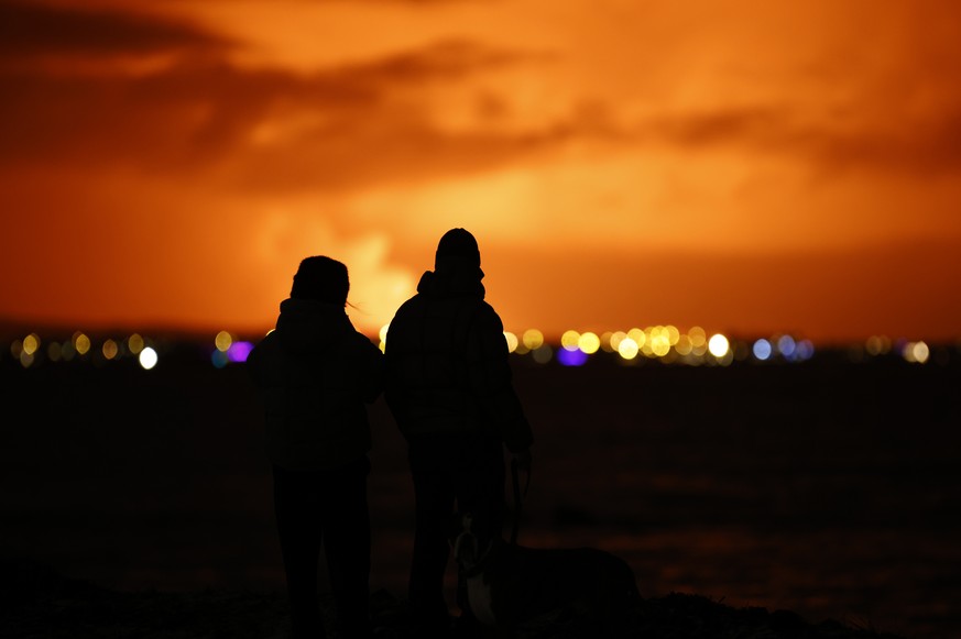 People watch as the night sky is illuminated caused by the eruption of a volcano on the Reykjanes peninsula of south-west Iceland seen from the capital city of Reykjavik, Monday Dec. 18, 2023. (AP Pho ...
