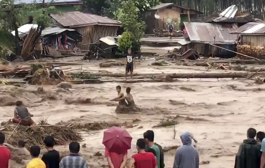 In this photo made from video by Aclimah Disumala, Friday, Dec. 22, 2017, villagers carry cross raging flood waters in Lanao del Norte, Zamboanga Pennisula, southern Philippines. A tropical storm has  ...