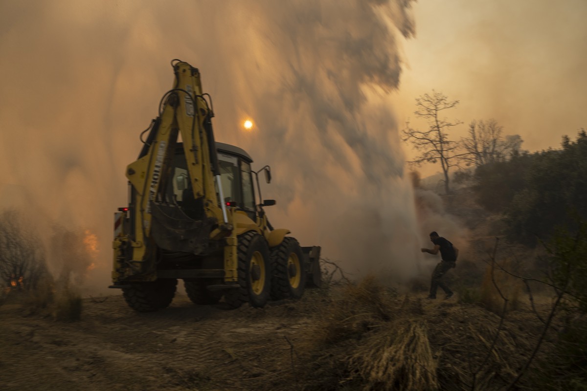 A bulldozer opens fire break as a local tries to avoid the water thrown by helicopter in Gennadi village, on the Aegean Sea island of Rhodes, southeastern Greece, on Tuesday, July 25, 2023. A firefigh ...