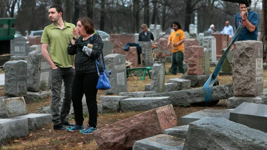 Schockierte Besucher betrachten die Schäden auf dem zerstörten Friedhof.