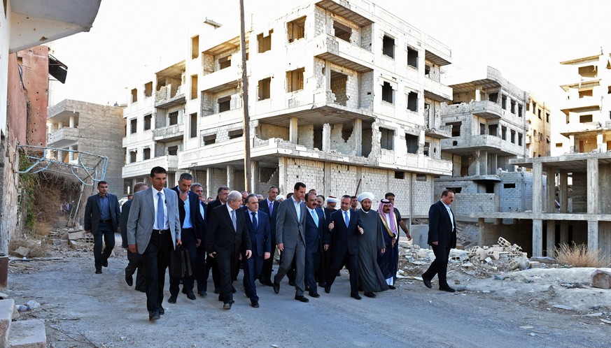 In this photo released by the Syrian official news agency SANA, Syrian President Bashar Assad, center, walks on a street with officials after performing the morning Eid al-Adha prayers in Daraya, a bl ...