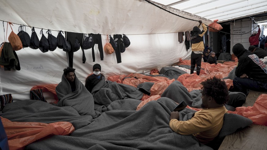 Migrants wrapped in blankets and waterproof bags lie on the deck of the Ocean Viking rescue ship, in the Strait of Sicily, in the Mediterranean Sea, Saturday, Nov. 5, 2022. (AP Photo/Vincenzo Circosta ...