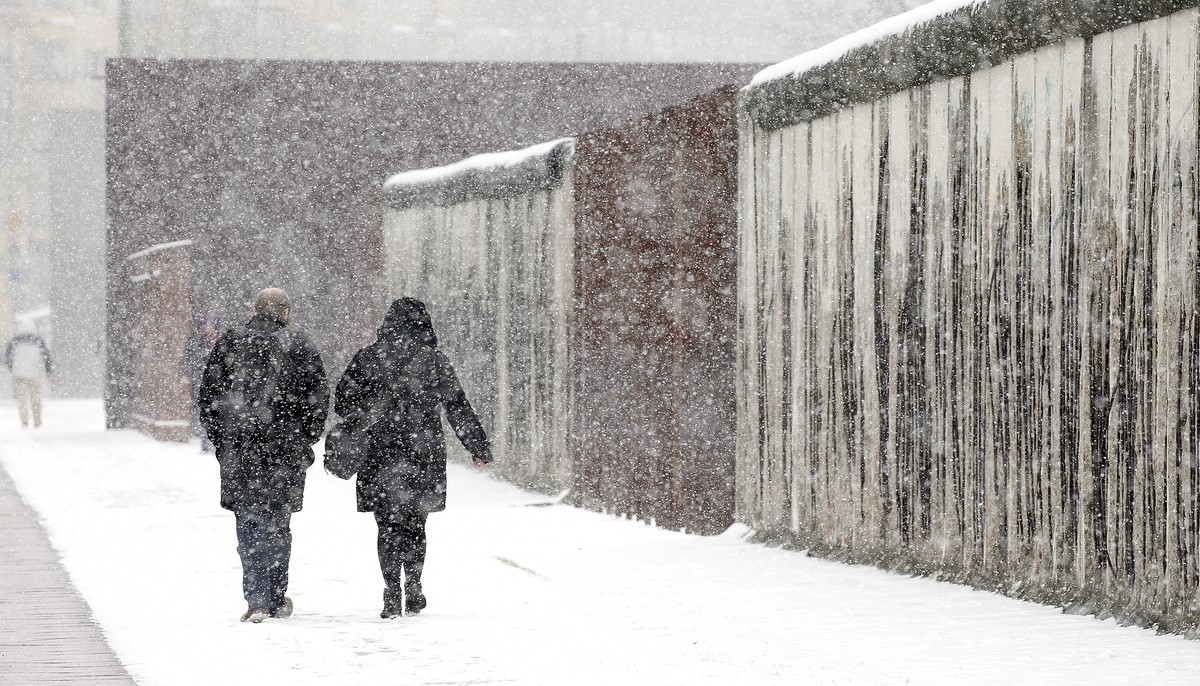 Two people walk pass remains of the Berlin Wall at the 'Mauerpark' memorial during snow fall in Berlin, Germany, Tuedsay, March 20, 2018. (Wolfgang Kumm/dpa via AP)