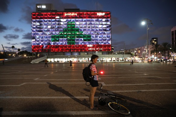 epaselect epa08585842 A person stands near the Tel Aviv Municipality building illuminated with the colors of the Lebanese flag as a sign of solidarity with the victims of the Beirut explosion, in Rabi ...