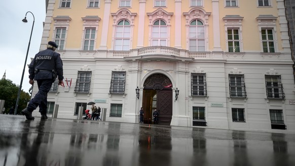 epa09509406 People walk along the Ballhausplatz square as two Austrian police officers stand in front of the Chancellery building in Vienna, Austria, 06 October 2021. Austrian prosecutors raided offic ...