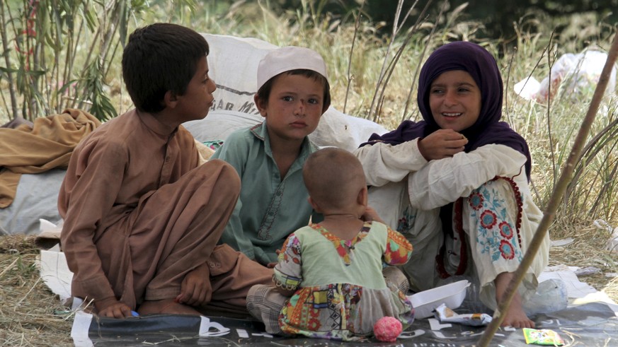 Displaced children sit under their tent's shade as they take refuge on a roadside after fleeing their flood-hit homes, in Charsadda, Pakistan, Monday, Aug. 28, 2022. International aid was reachin ...