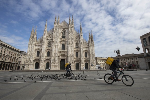 Two workers ride past the gothic cathedral in downtown Milan, Italy, Tuesday, March 31, 2020. The new coronavirus causes mild or moderate symptoms for most people, but for some, especially older adults and people with existing health problems, it can cause more severe illness or death. (AP Photo/Luca Bruno)