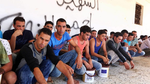 epa04902540 Some of the refugees rescued after their boats capsized rest in front of a wall with the words reading in Arabic &#039;Martyrs&#039;, after being detained by authorities in Zuwarah, Libya, ...