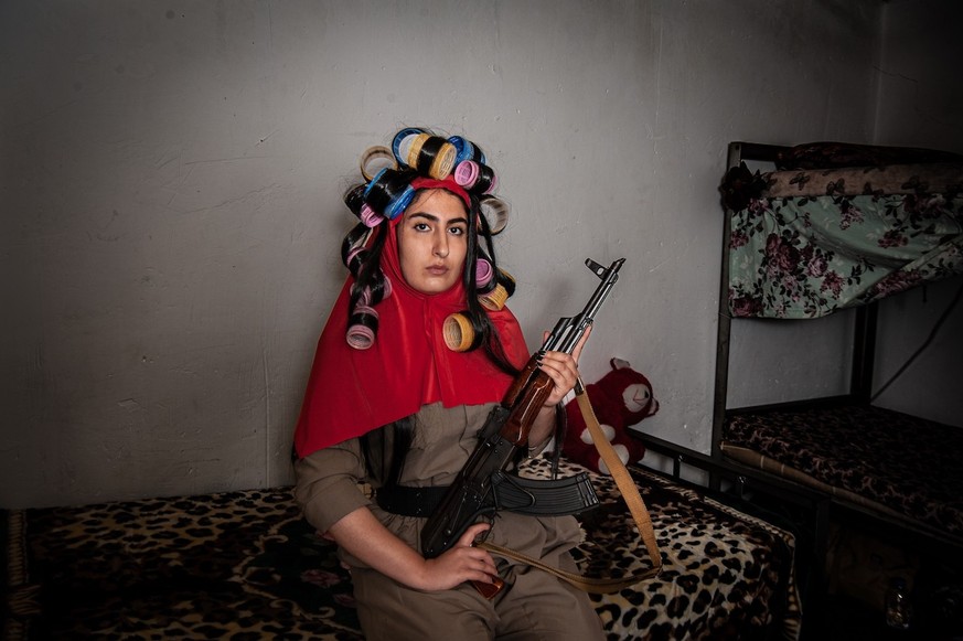 A young Iranian Kurdish soldier is captured in her small dormitory with her hair flowing from her veil, looking wild and messy.  This representation emphasizes her right to exist and breathe and see...