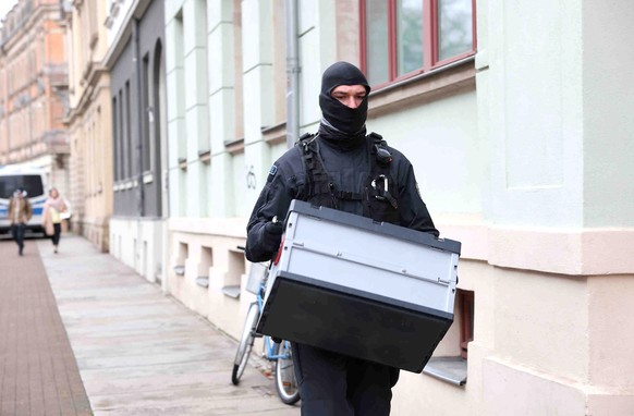 epa09643044 A police officer carries a box during a raid in front of a residential building in Dresden, Germany, 15 December 2021. Police and special forces of the State Criminal Police Office (LKA) s ...