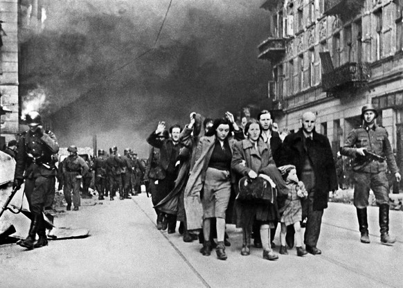 Während die Wehrmacht Häuser in Brand setzt, führen SS-Männer nach dem Aufstand im Warschauer Ghetto 1943 Juden ab, die nach Auschwitz deportiert werden.