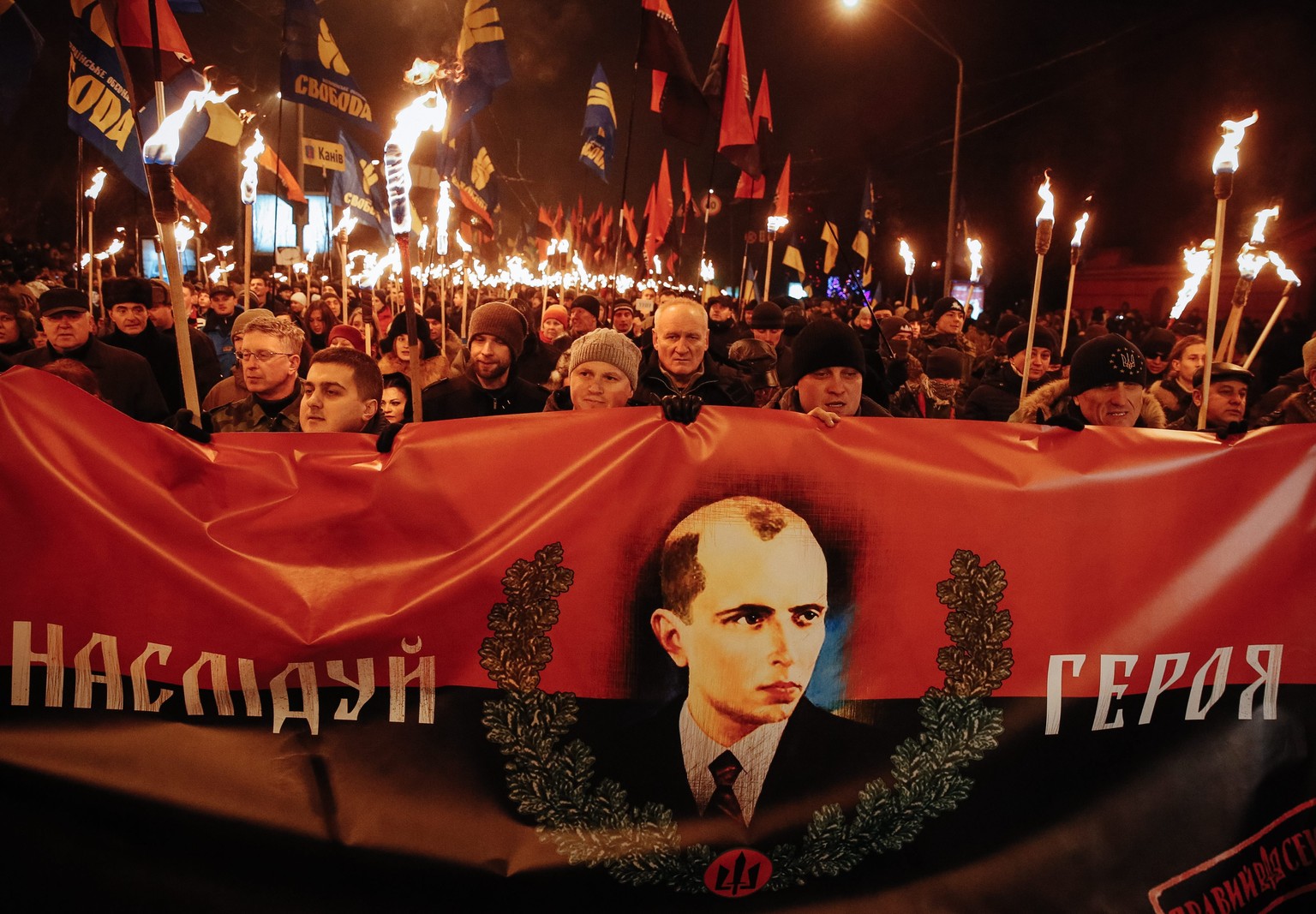 epa04544637 Supporters of the Ukrainian nationalist parties &#039;Svoboda&#039; and &#039;Right Sector&#039; carry torches and a banner with a portrait of Stepan Bandera during a march to mark the 106 ...