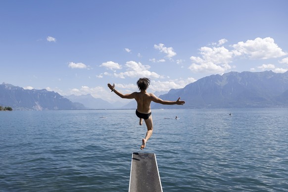 epaselect epa10734761 A man jumps into the lake on a warm summer day on the shores of Lake Geneva in front of the Swiss Alps mountains, in Vevey, Switzerland, 08 July 2023. EPA/CYRIL ZINGARO