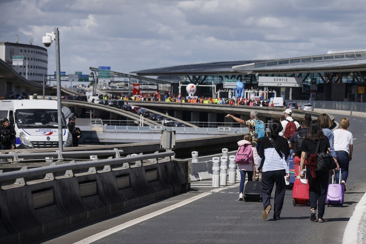 Des voyageurs arrivent à pied à l'aéroport de Roissy-Charles de Gaulle tandis que des travailleurs de l'aéroport manifestent, vendredi 1er juillet 2022 à l'aéroport de Roissy, au nord d ...