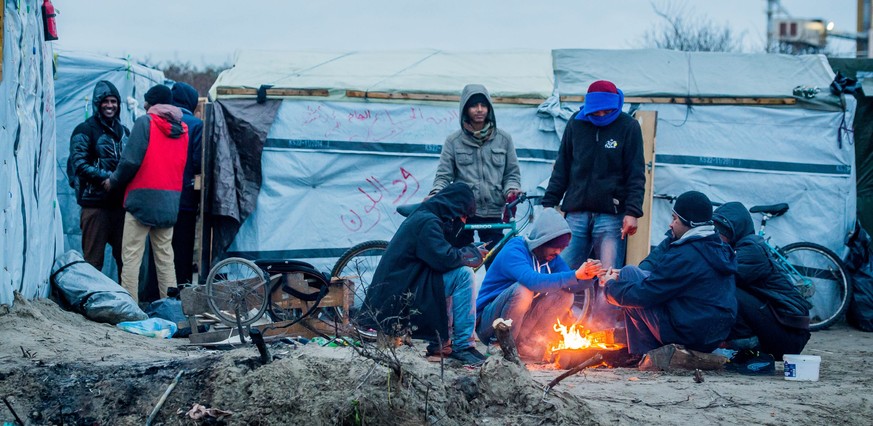 epa05080919 Refugee warm around a wood fire in the refugee camp during Christmas Day in the camp called &#039;The Jungle&#039; in the port of Calais, France, 25 December 2015. Part of Calais migrant c ...
