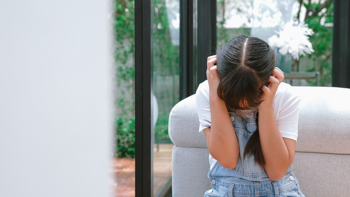 Stressed and unhappy young girl huddle in corner, cover her ears blocking sound of her parent arguing in background. Domestic violence at home and traumatic childhood develop to depression. Synchronos ...