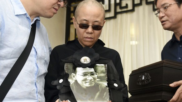 In this July 15, 2017, file photo provided by the Shenyang Municipal Information Office, Liu Xia, center, wife of jailed Nobel Peace Prize winner and Chinese dissident Liu Xiaobo, holds a portrait of  ...