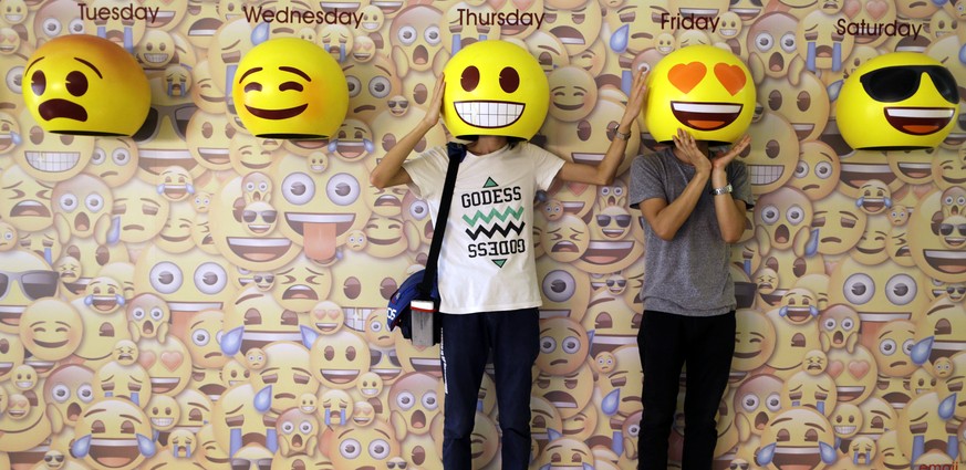 In this Wednesday, May 18, 2016, 2016, passers-by pose for photos with emoji masks fixed onto a wall at a shopping mall in Guangzhou in south China&#039;s Guangdong province. Emoji icons are popularly ...