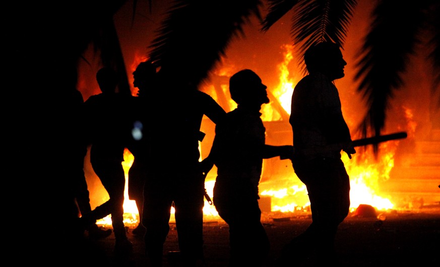 FILE - In this Friday, Sept. 21, 2012 file photo, Libyan civilians watch fires at an Ansar al-Shariah Brigades compound, after hundreds of Libyans, Libyan Military, and Police raided the Brigades base ...