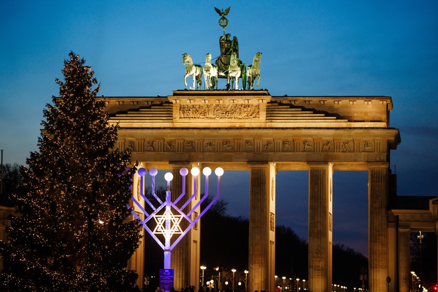 epa12596897 An illuminated Christmas tree (L) stands in front of a Hanukkah menorah (C) and the Brandenburg Gate in Berlin, Germany, 16 December 2025. EPA/CLEMENS BILAN