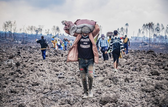 epaselect epa09234046 A Congolese porter helps people evacuate across cooled lava from the town of Goma in the aftermath of Mount Nyiragongo volcano over Goma, Democratic Republic of the Congo, 26 May ...